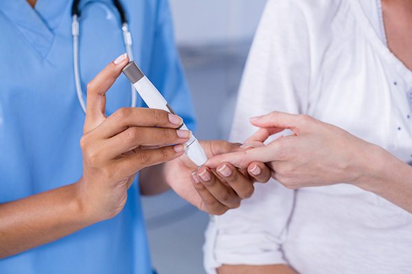 Mid section of doctor examining pregnant womans blood sugar